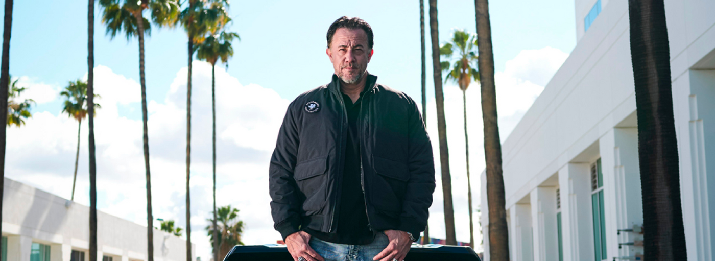 Man standing outdoors with palm trees and a building in the background