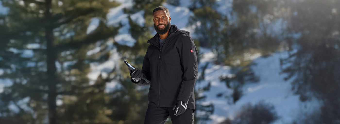 Man in black winter coat and gloves standing in a snowy forest