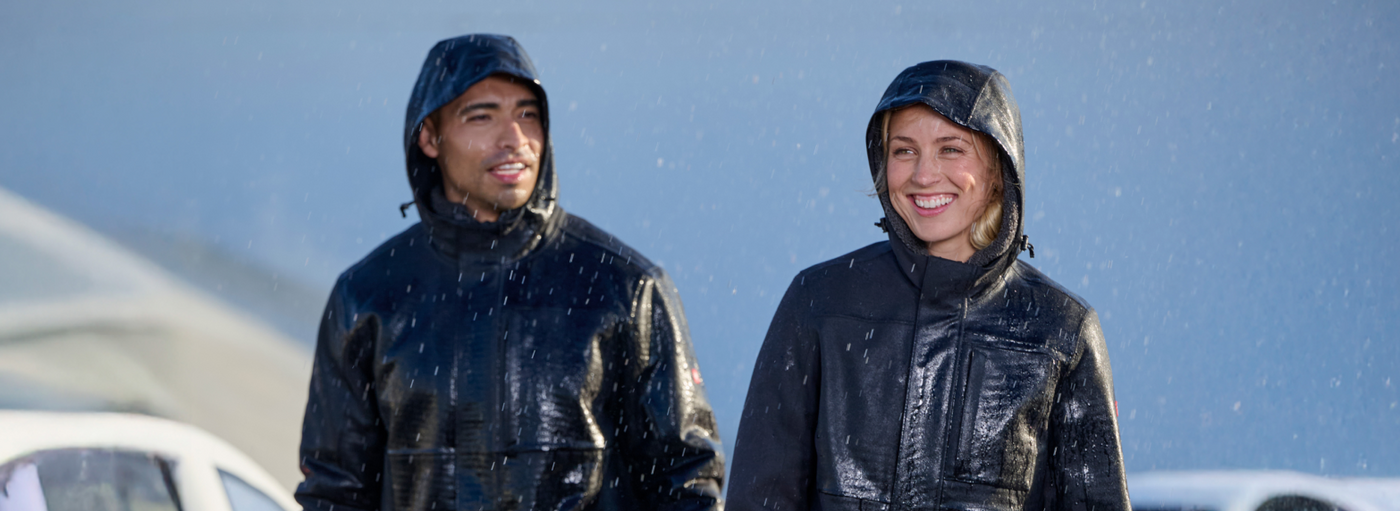Two people wearing raincoats standing outdoors with a clear blue sky.