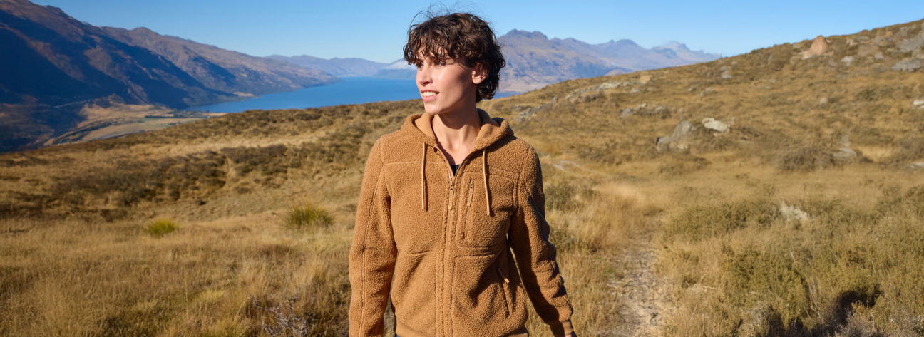 Person standing in a scenic landscape with mountains and a lake.