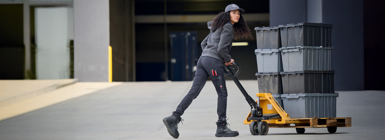 Person pushing a pallet truck with stacked containers in an industrial setting