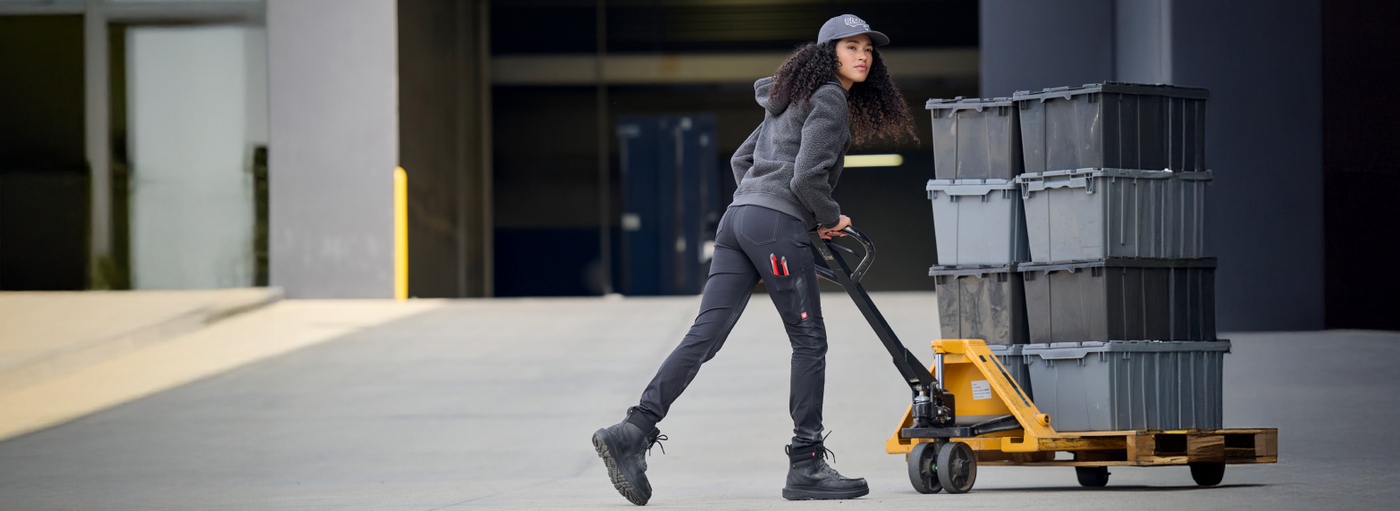 Person pushing a pallet truck with stacked containers in an industrial setting