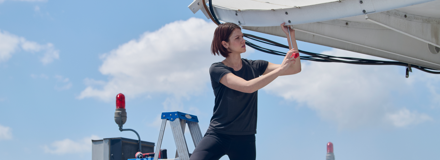 Person working on a satellite dish with a clear blue sky in the background