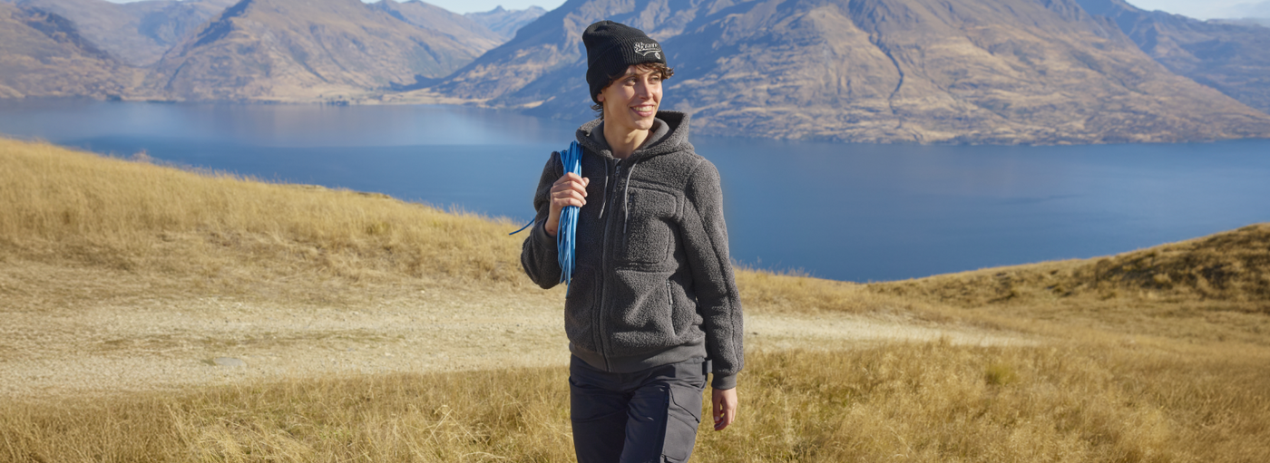Woman hiking in gray fleece jacket near mountain lake.