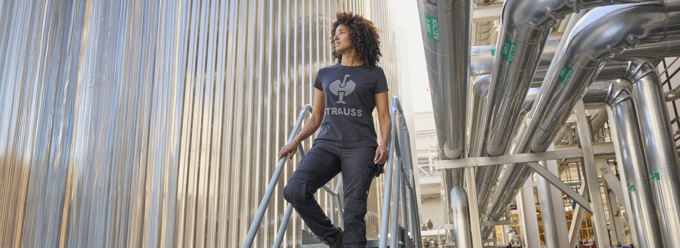 Woman wearing black work pants in industrial setting with steel tanks
