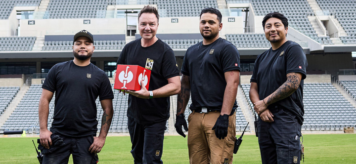 Four men in black uniforms standing on a sports field with a red box.