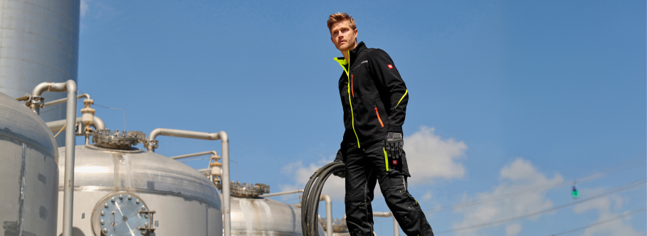 Person in a high-visibility work outfit standing next to industrial equipment with a clear blue sky in the background.