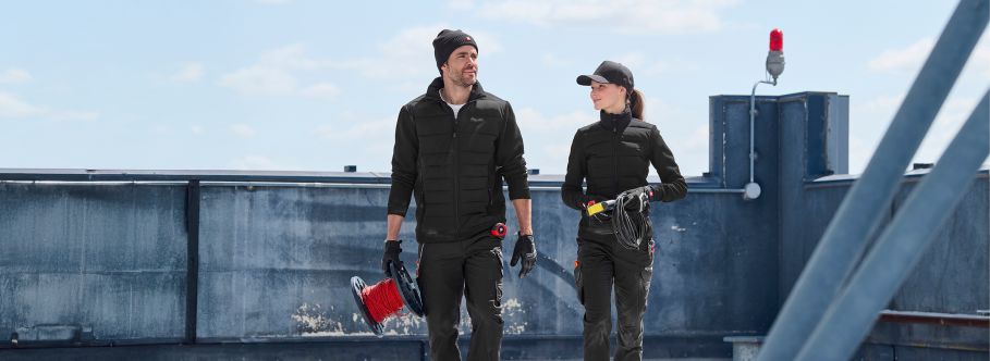 Two people on a rooftop with tools, wearing black outfits.