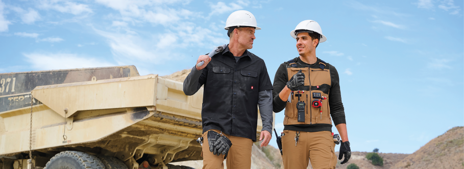 Two workers in hard hats walking next to a large piece of construction equipment with a clear blue sky in the background.