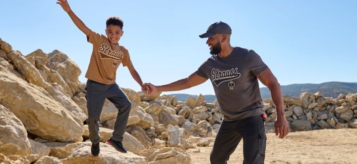 Two people holding hands on a rocky landscape with mountains in the background