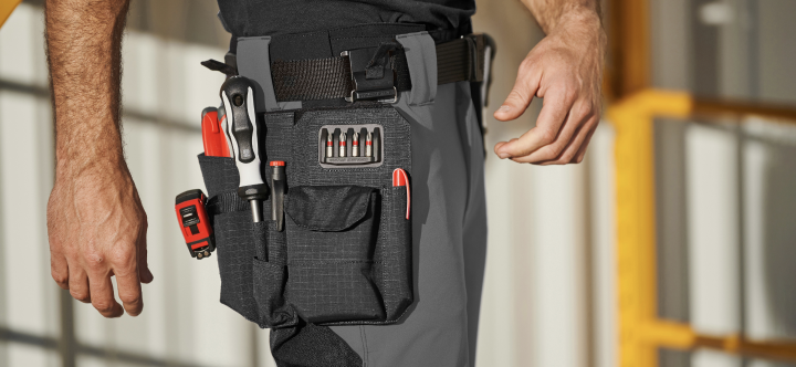A close-up view shows a black multi-pocket tool bag attached to a belt at waist level, filled with screwdriver bits and hand tools.