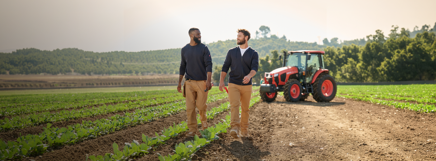 Two men walking on a field with a tractor in the background