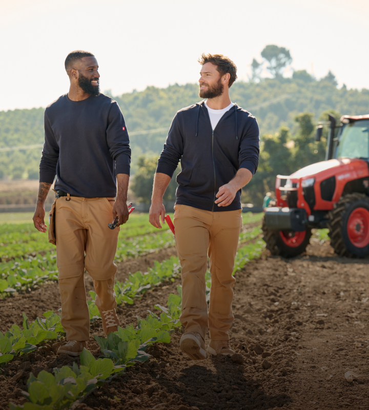 Two men walking on a field with a tractor in the background