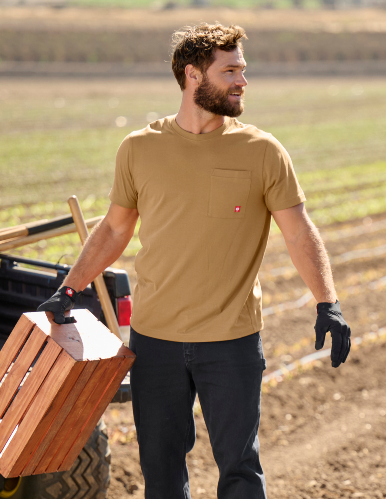 Man in a brown shirt carrying a wooden crate in a field