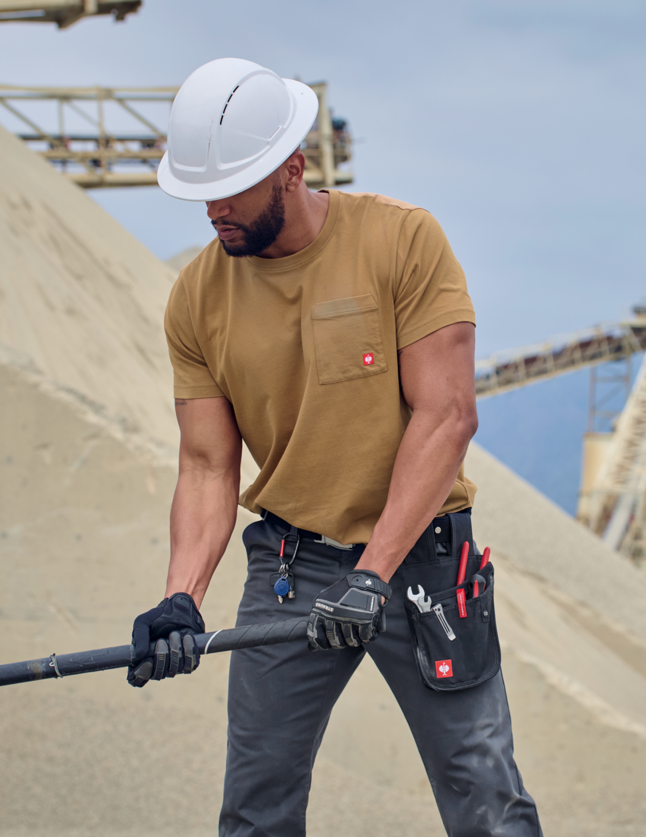Man in a brown shirt with hard hat and tool belt on a construction site