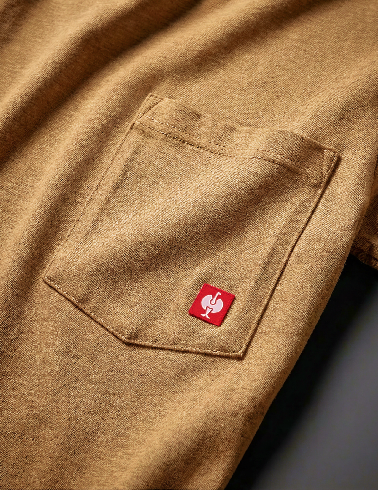 Close-up of a brown shirt with a red logo on the chest pocket.