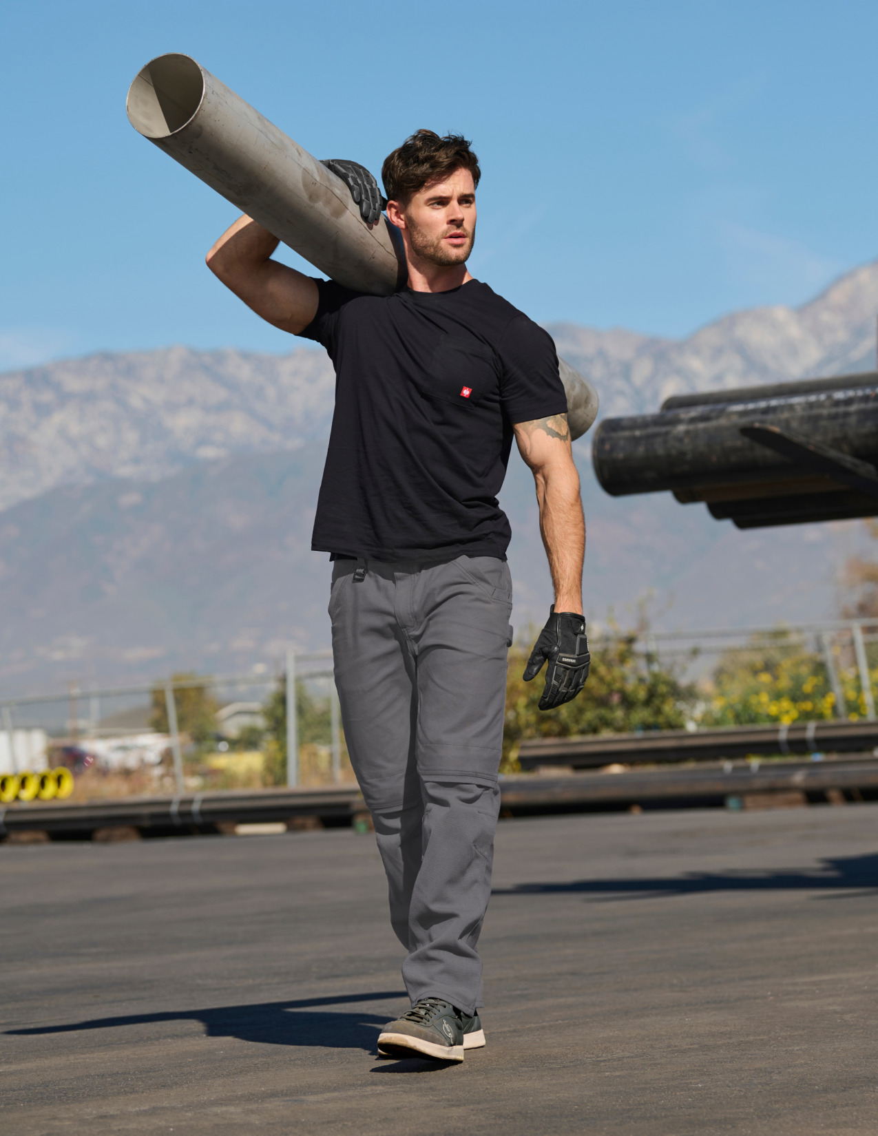 Man carrying large pipes outdoors with mountains in the background