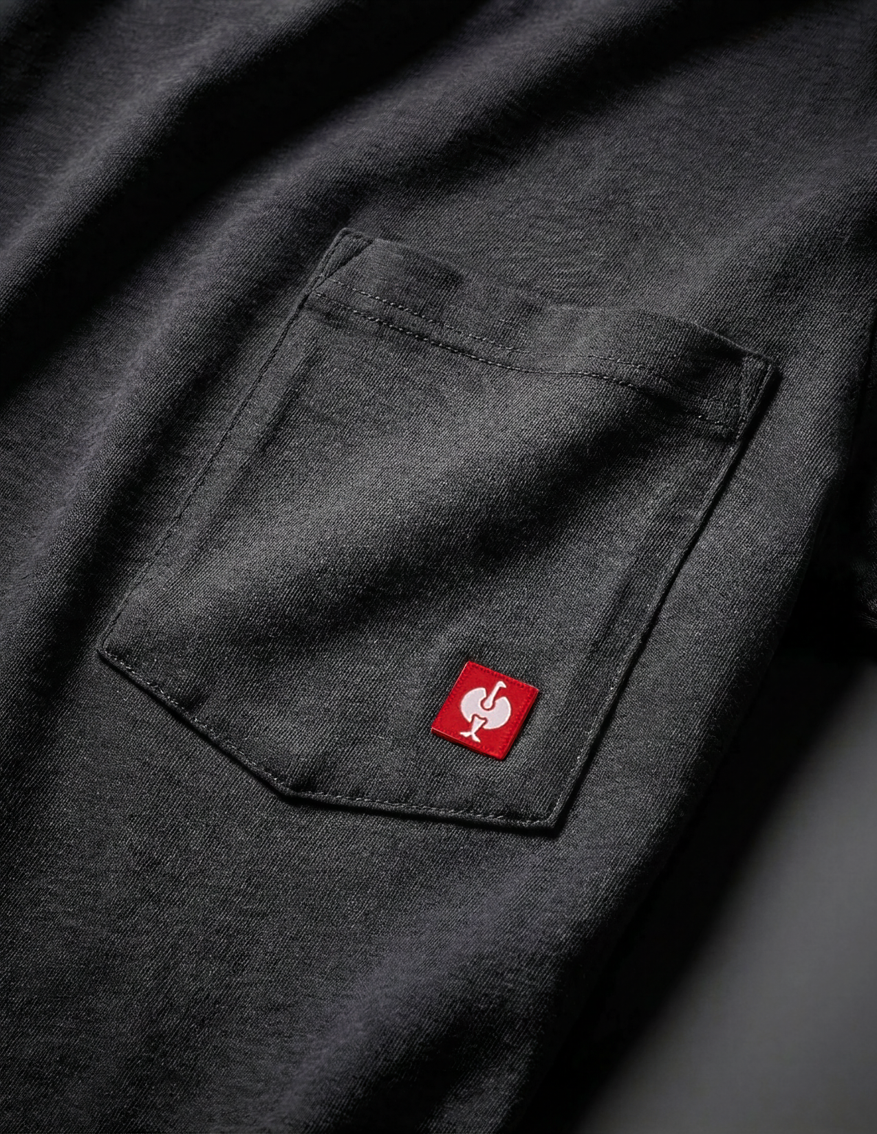 Black shirt with a red logo on the chest pocket against a dark background