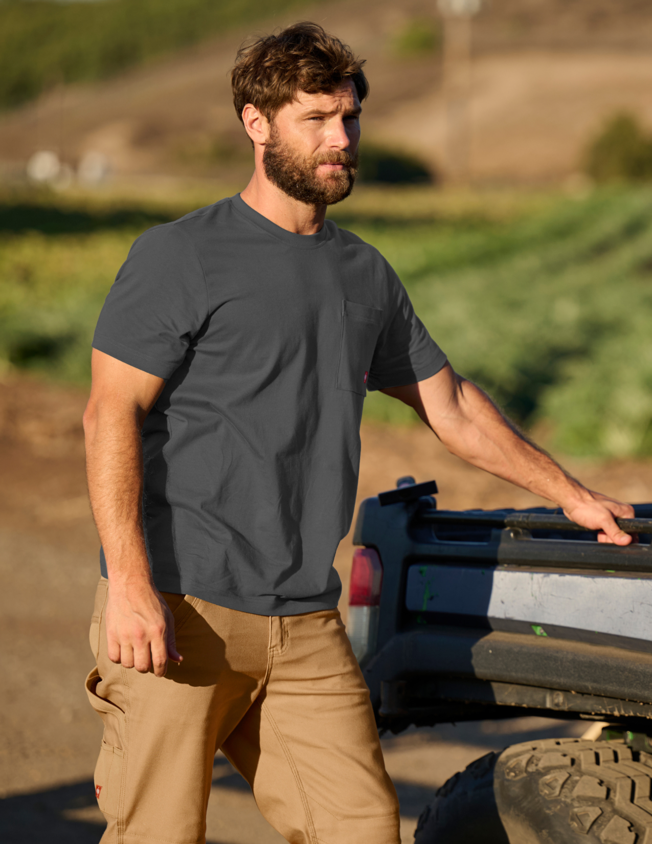 Man in a gray t-shirt and beige pants standing next to a truck in an outdoor setting