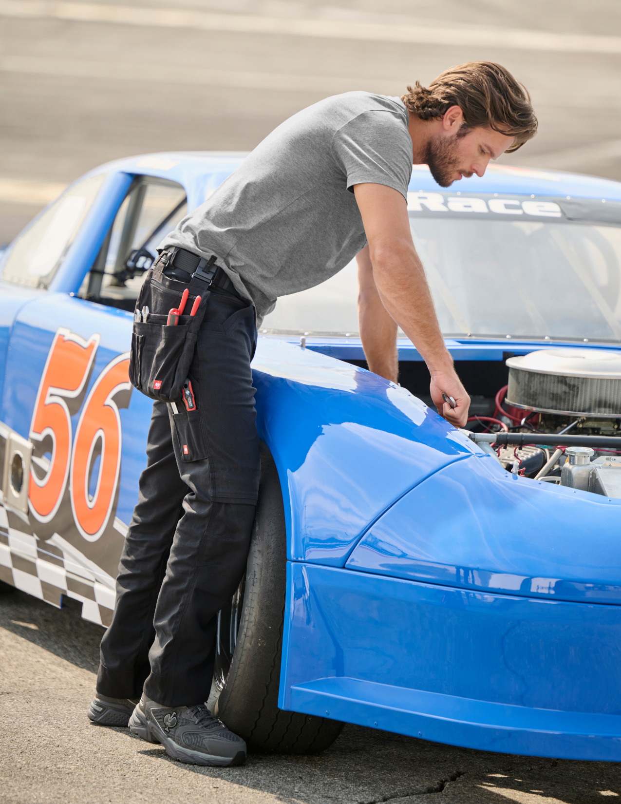 Person in a grey shirt working on a blue race car with number 56 on a track