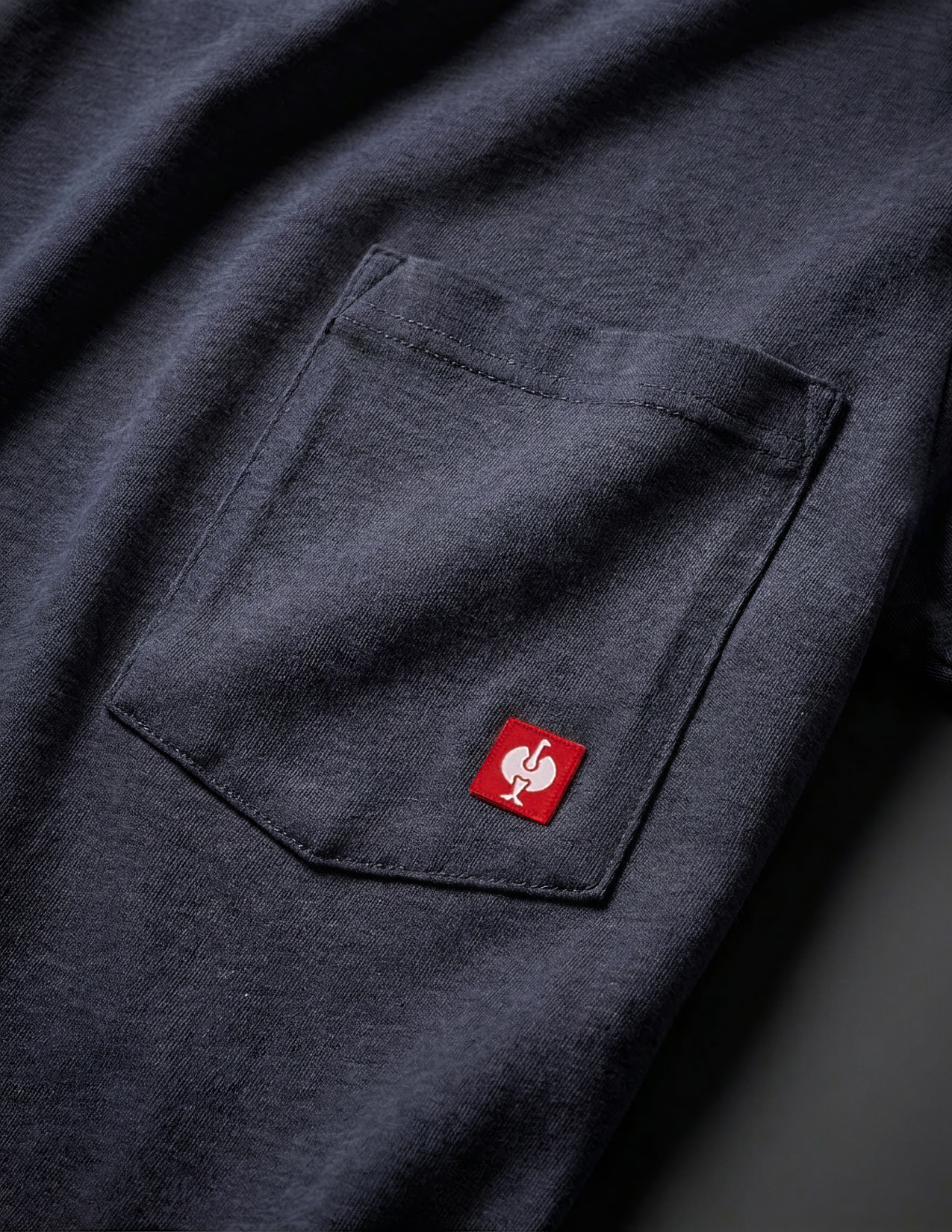 Close-up of a dark blue shirt with a red logo on the chest pocket.