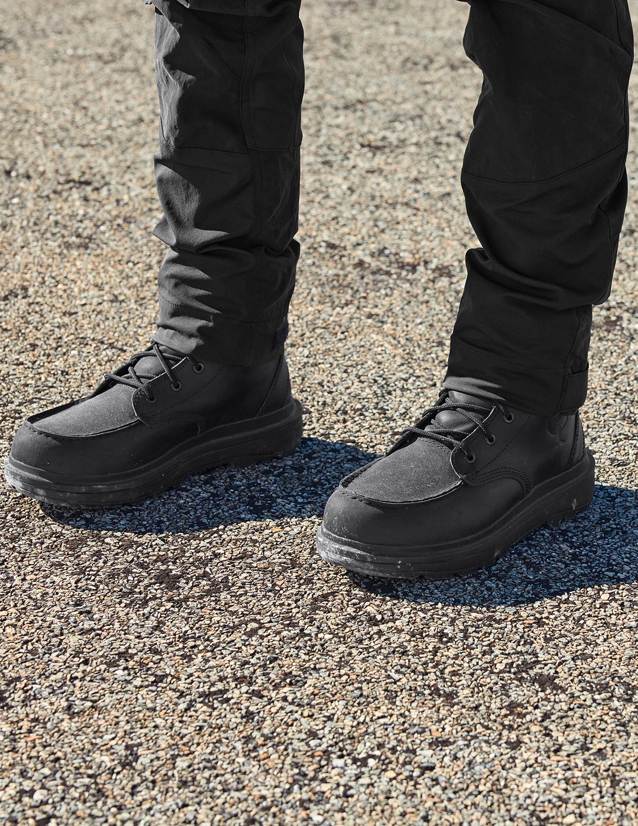 Black boots worn with black pants on a textured ground