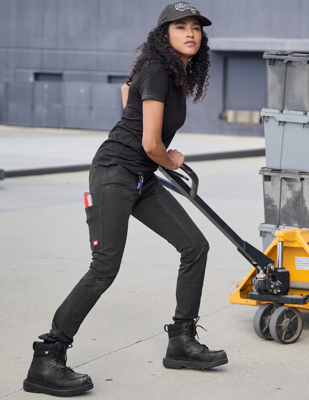 Person pushing a hand truck with a container on a concrete surface.