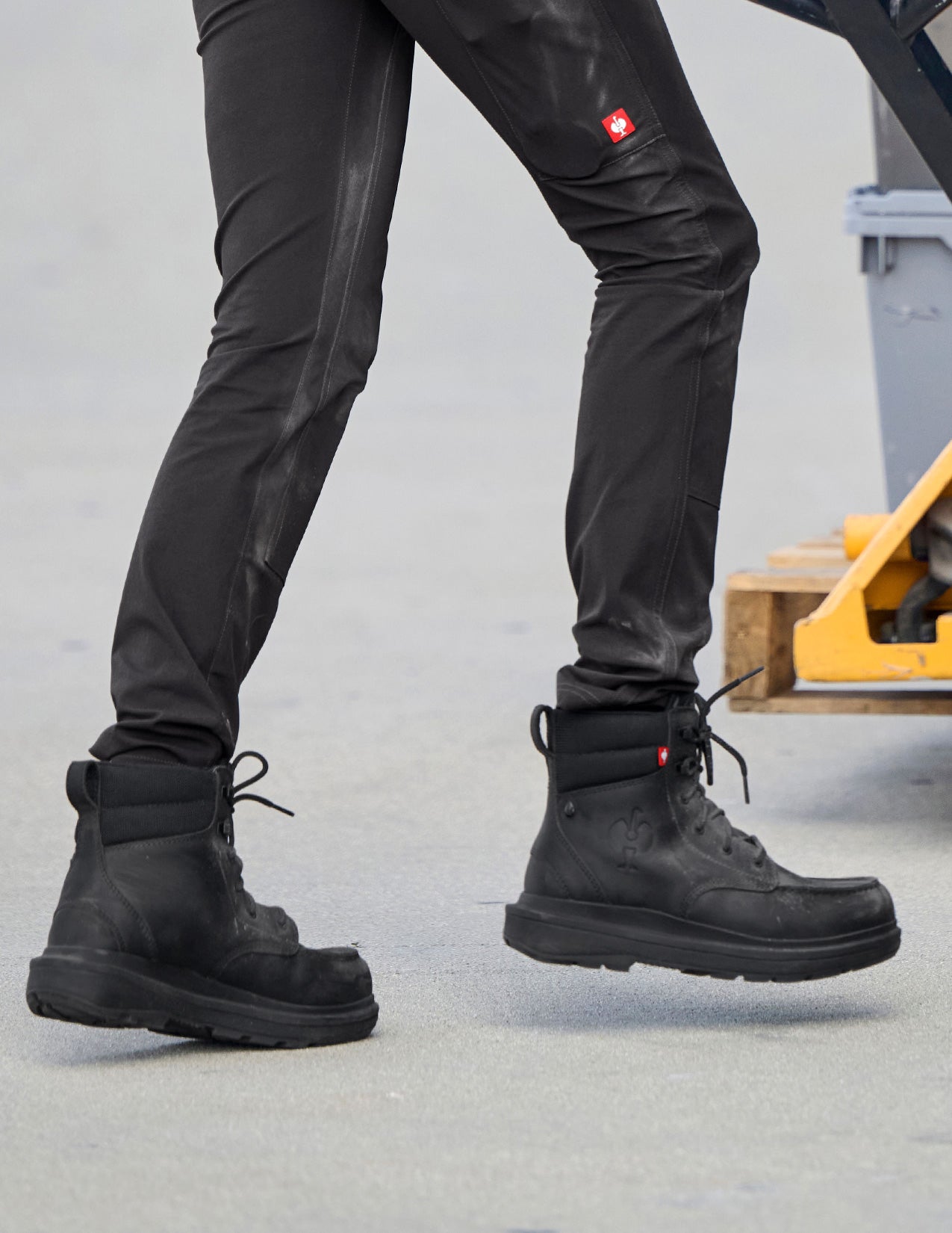 Person wearing black boots and pants with a visible brand logo on a concrete floor.