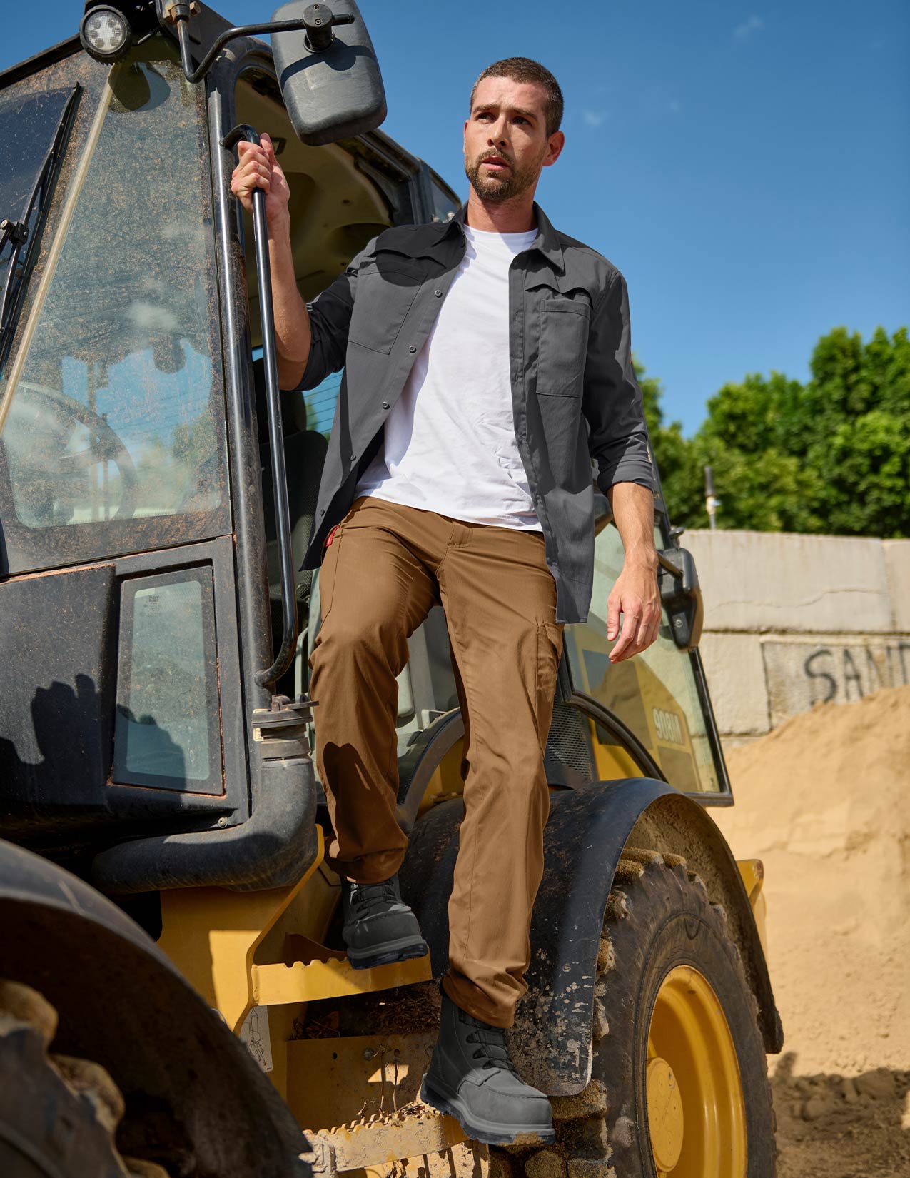Man standing on a piece of construction equipment with a clear sky and greenery in the background