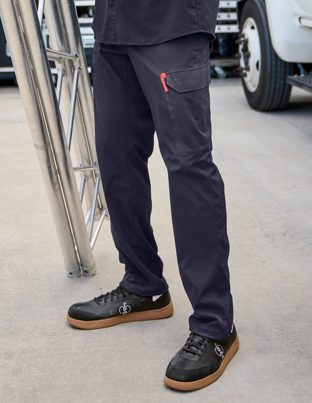 Person wearing dark blue pants and black shoes on a concrete surface with a vehicle in the background