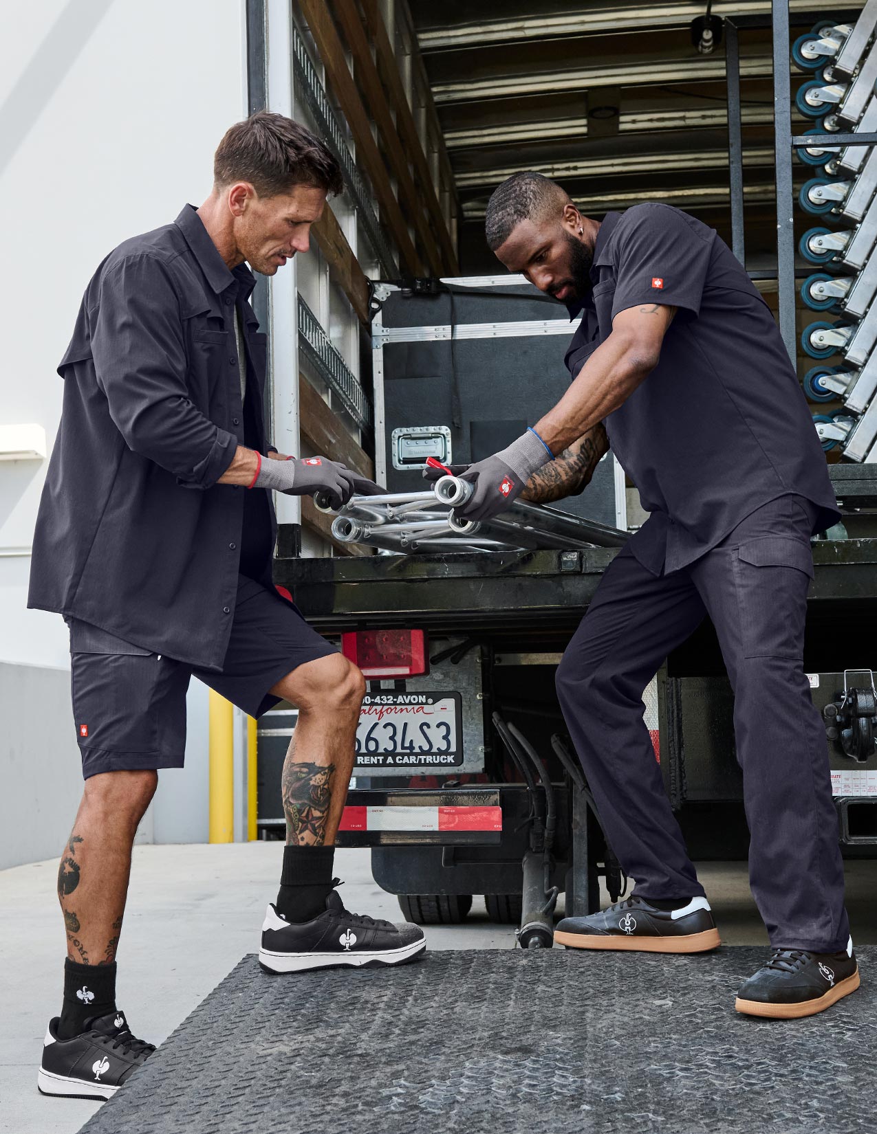 Two men working on a truck with tools, both wearing dark blue outfits