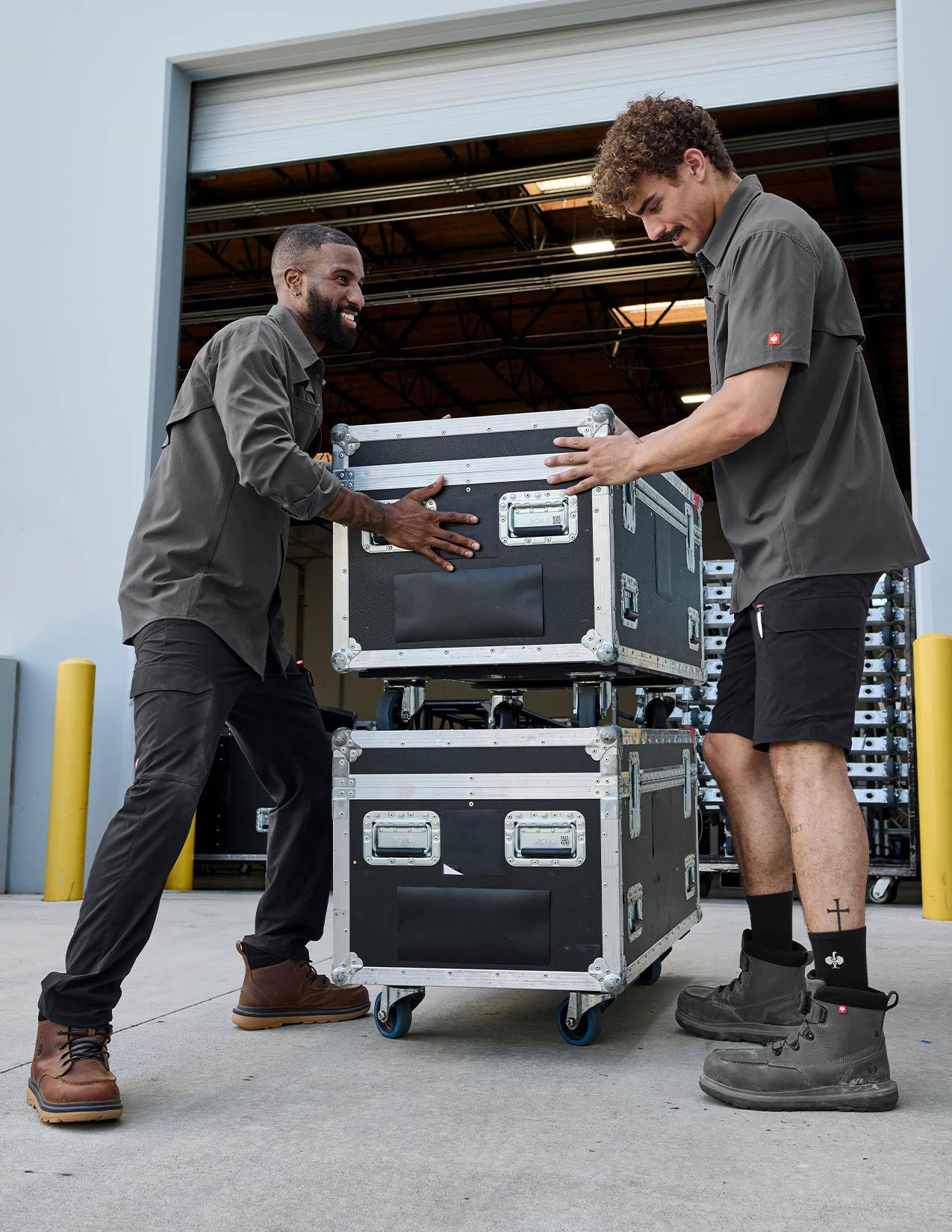 Two men handling large black equipment cases outside a building