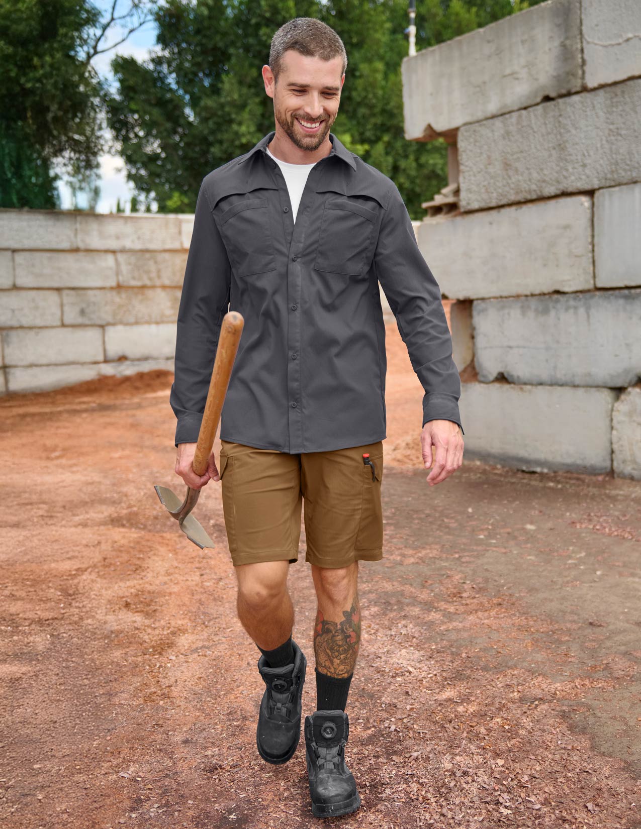 Man wearing a grey shirt and brown shorts, holding a shovel, standing outdoors.