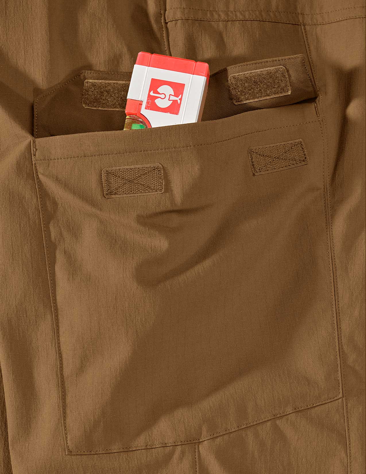 Brown pants with a spirit level in the pocket featuring a logo.