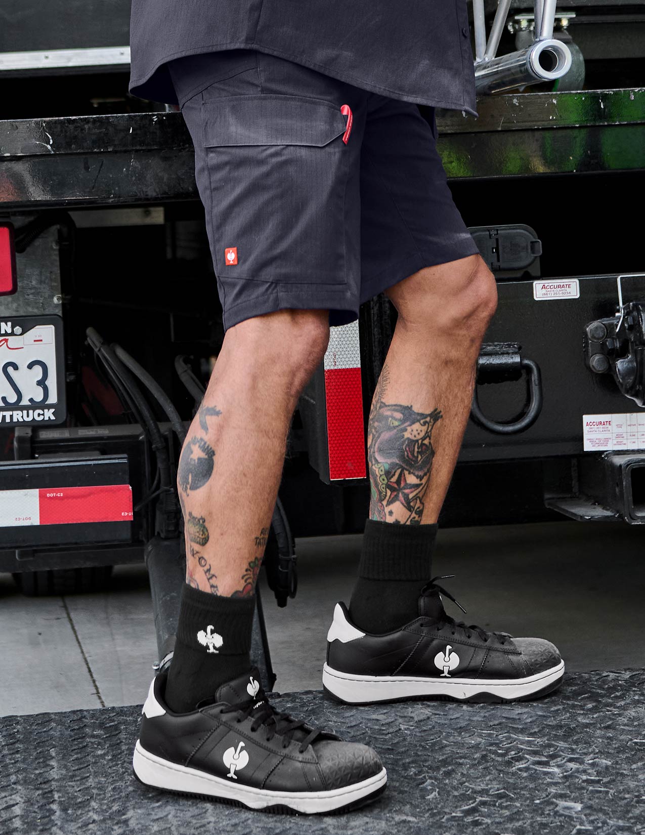 Person wearing dark blue shorts, black and white socks, and shoes with a visible brand logo in front of a truck.