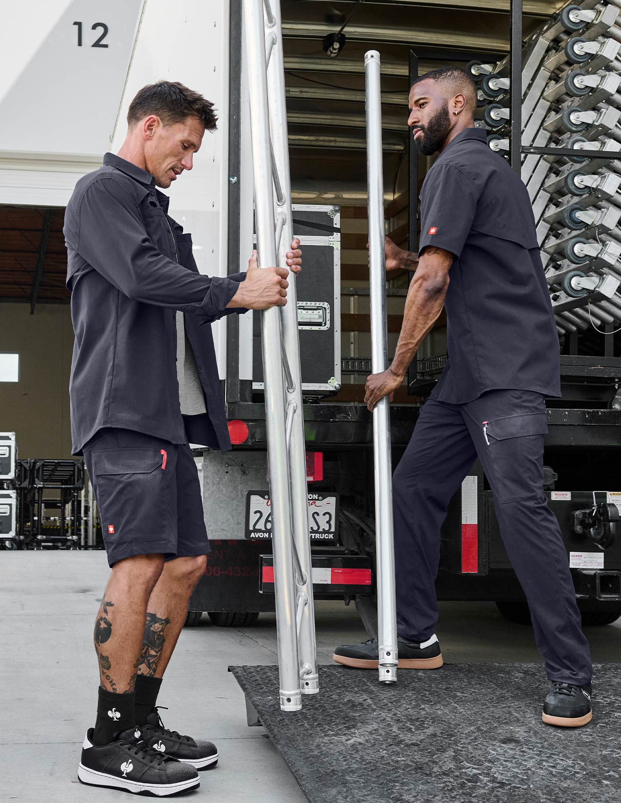 Two men in dark blue uniforms unloading metal poles from a truck.