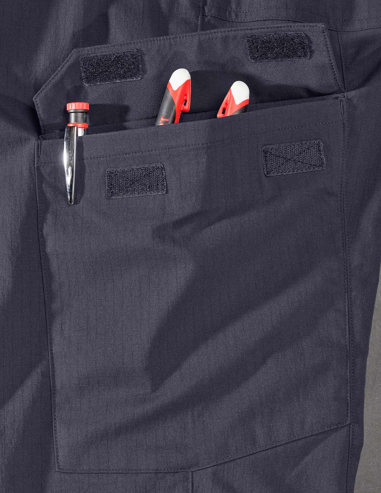 Dark blue pants with a pocket containing tools on a gray background
