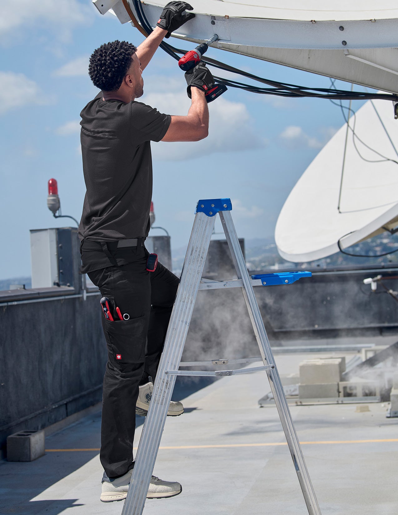Person on a ladder working on a satellite dish on a rooftop.