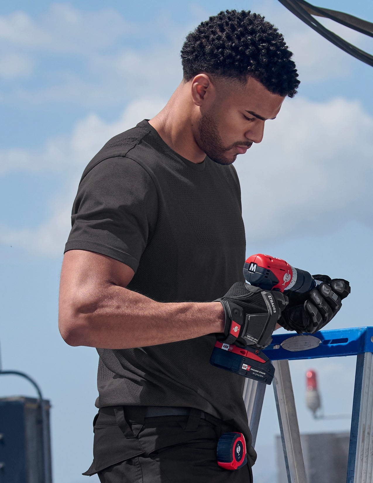 Man using a power drill with a clear blue sky background.