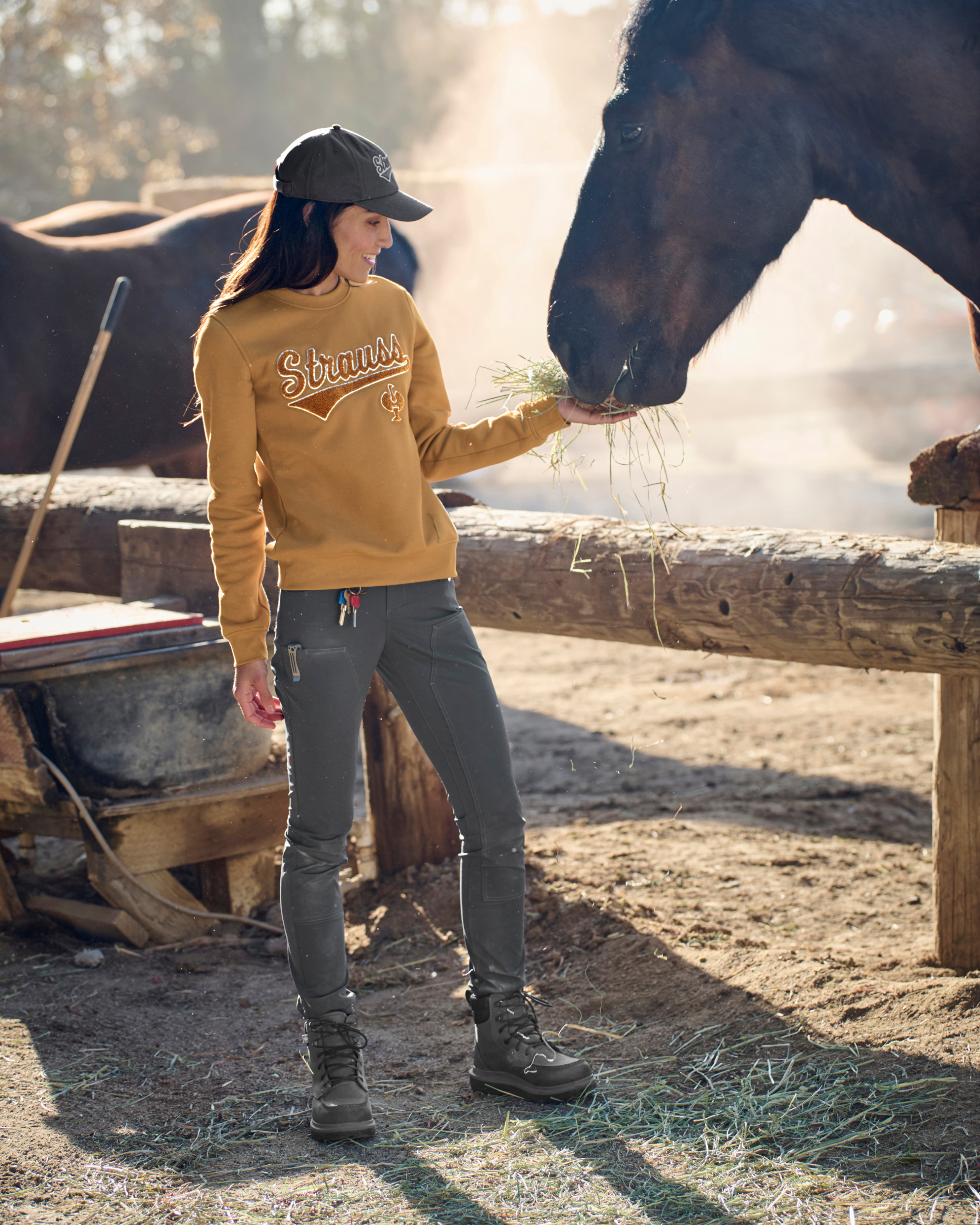 Woman in a yellow sweatshirt and gray pants feeding a horse in a stable.