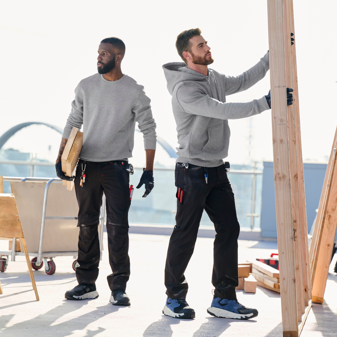 Two men in gray hoodies and black pants working on a wooden structure outdoors.