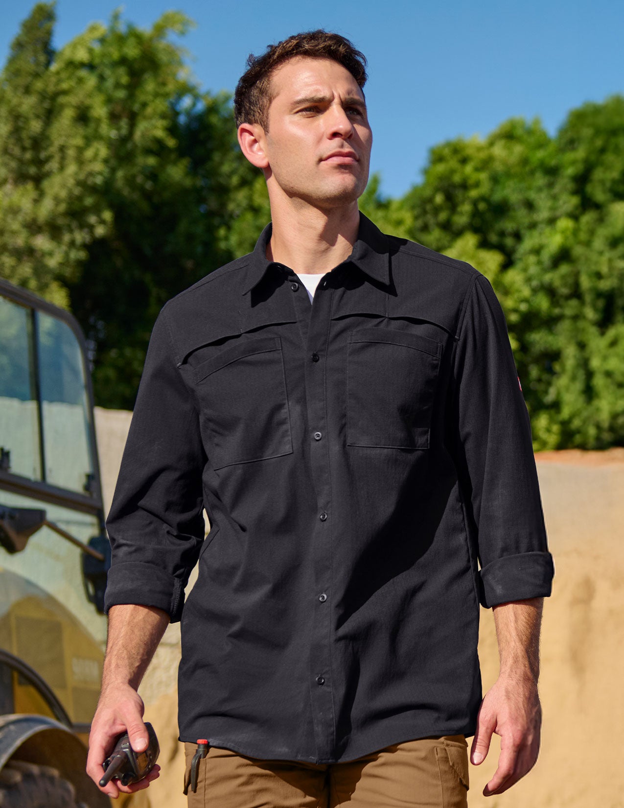 Man wearing a black shirt outdoors with greenery in the background