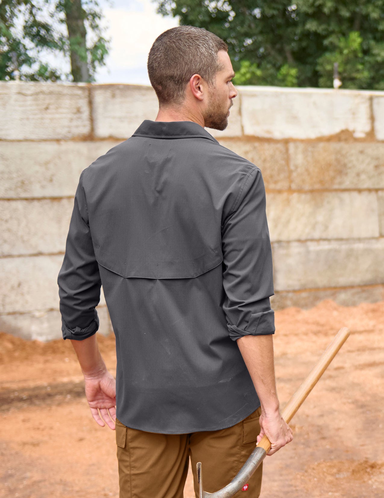 Man wearing a gray shirt and brown pants holding a tool outdoors.