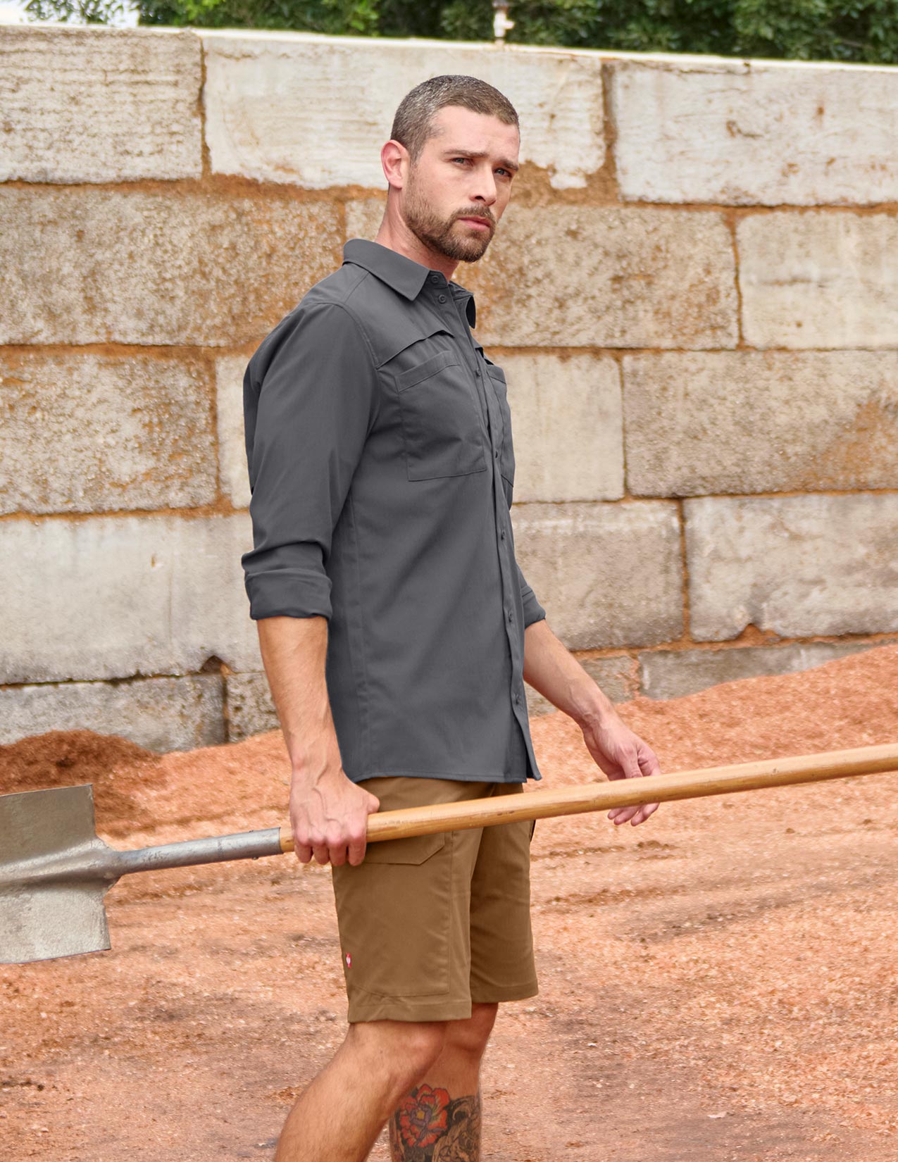 Man holding a shovel against a stone wall background