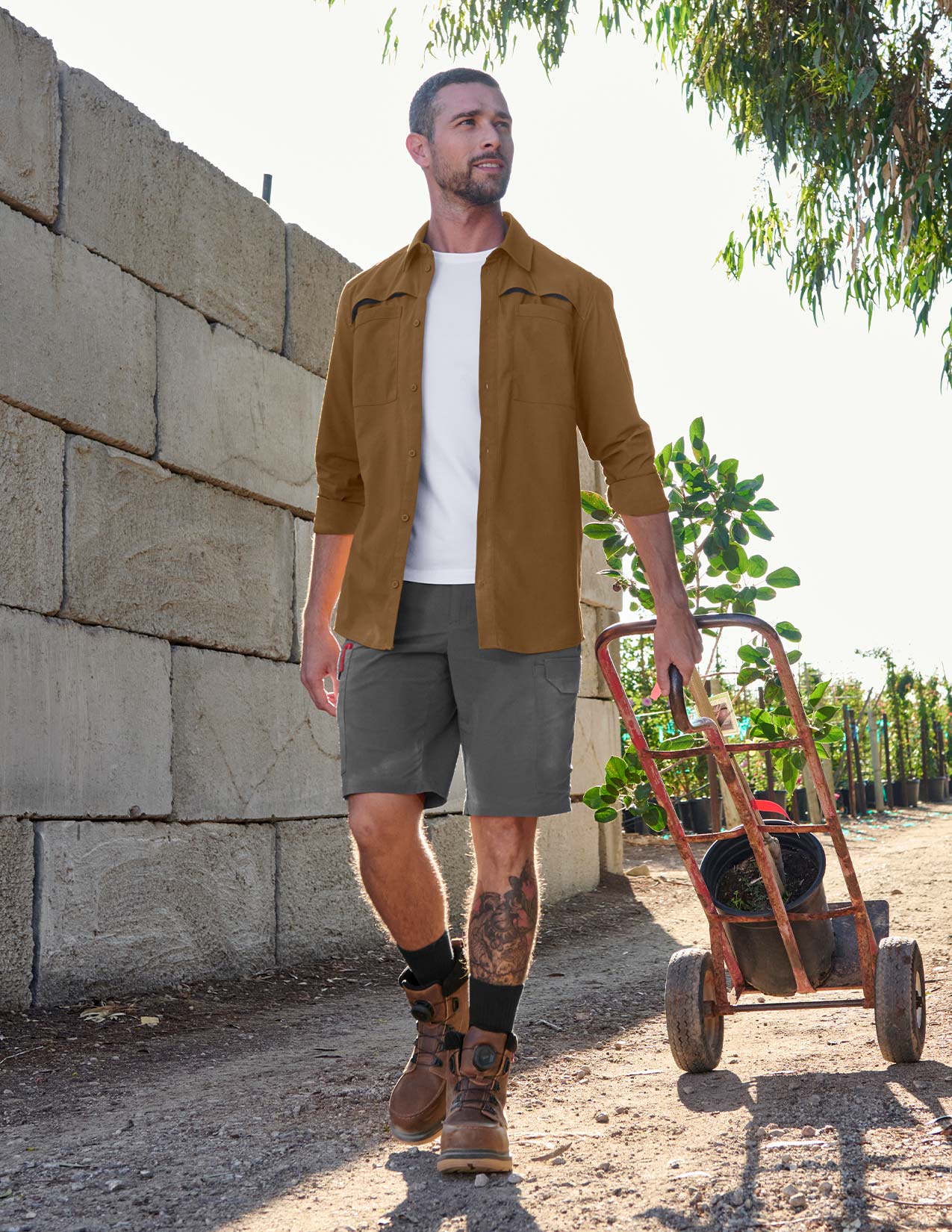 Man pushing a dolly with plants against a stone wall