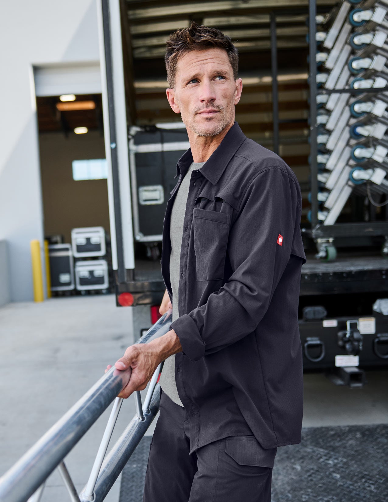 Man in a dark blue work shirt standing next to a truck with equipment in an industrial setting