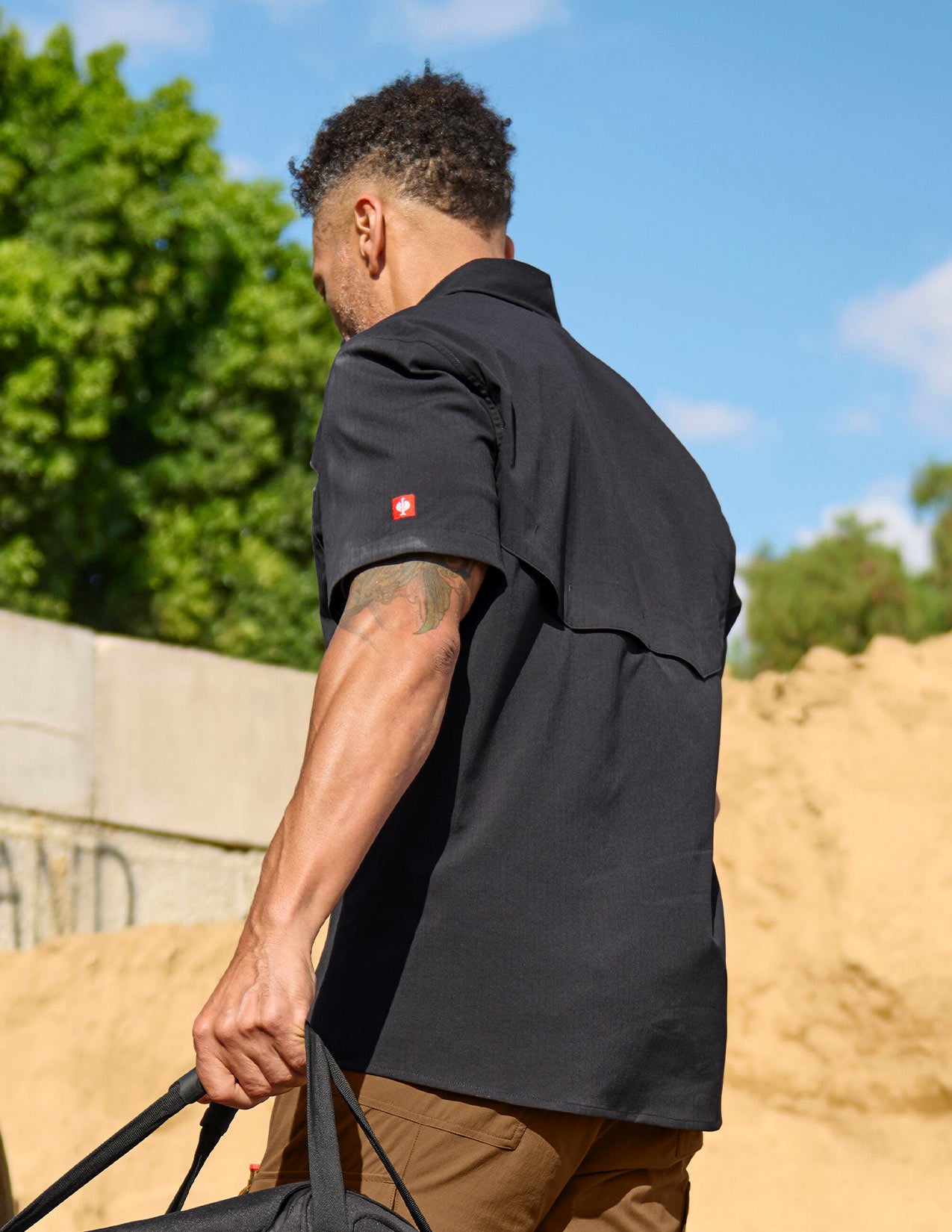 Man in a black short sleeved Work Shirt shown from behind