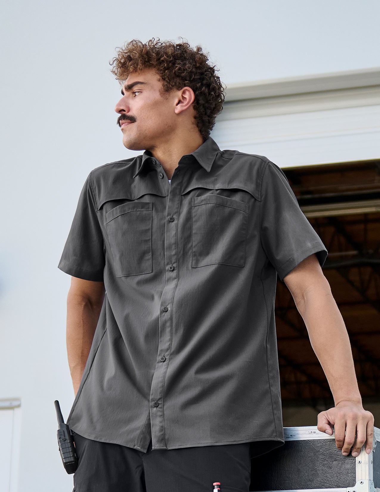 Man in grey work shirt leans against a box