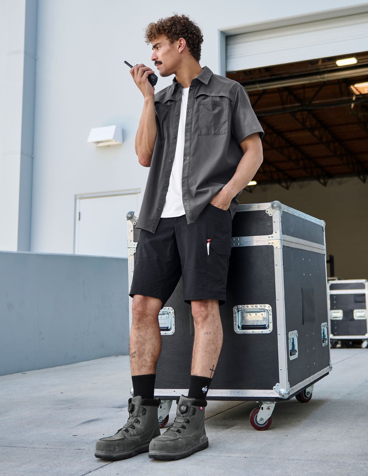 Man with open grey work shirt leans against a box, holding a radio