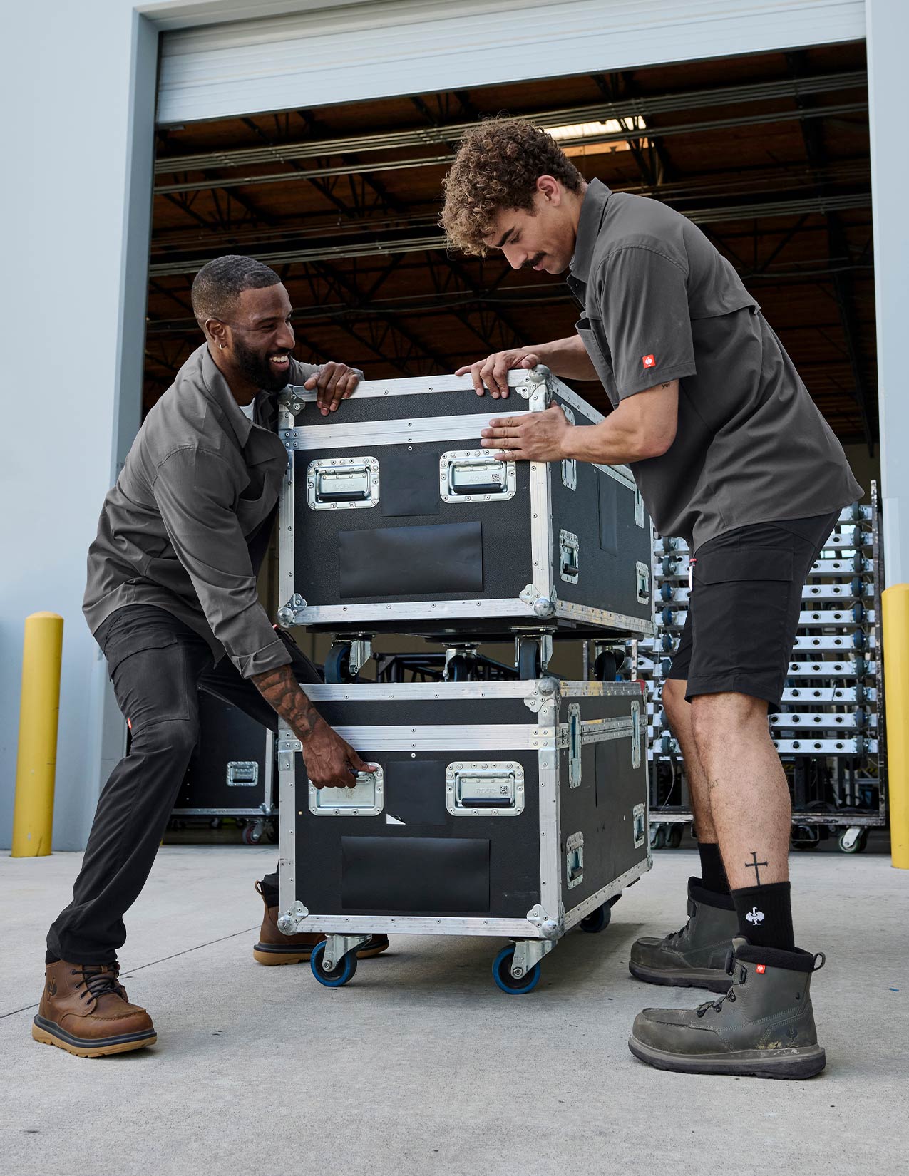 Two men in grey shirts and black pants. In the middle are two crates.